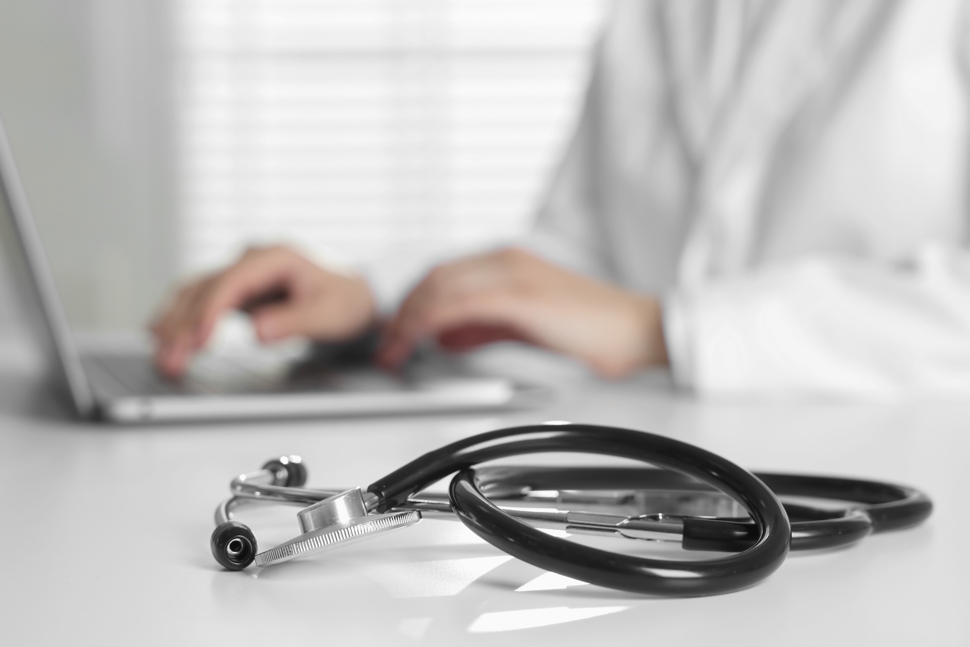A stethoscope resting on a desk while a healthcare administrator manages international nurse placements on a laptop.